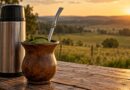 Cuia de chimarrão com bomba de inox e erva-mate ao lado de uma garrafa térmica sobre uma mesa de madeira